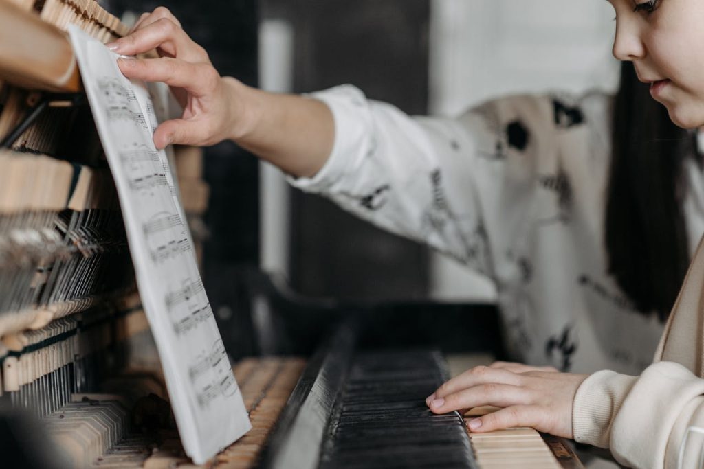 Young girl learning piano indoors, focusing on sheet music and hand placement.